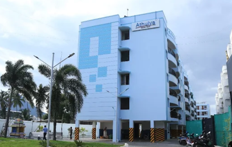 Alt Text:
Exterior view of the multi-story, light blue and white Athulya Senior Care building in Thudiyalur, featuring prominent branding near the top and palm trees along the front driveway.