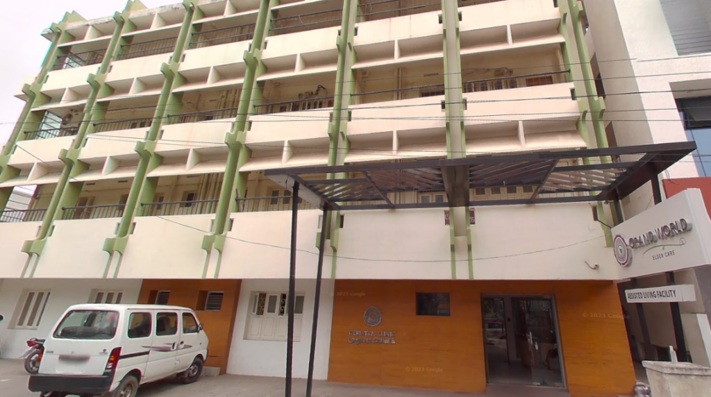 Exterior view of the multi-story Grand World Elder Care building in Ram Nagar, featuring green support pillars and a covered entryway signboard.